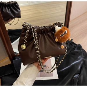 Detail of dark brown pleated bucket bag with gold chain strap and plush monster charm