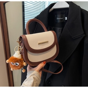 Détail du sac selle beige et marron avec breloque en fourrure et barre dorée chic