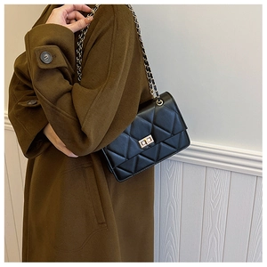Détail d'un sac bandoulière noir matelassé avec chaîne dorée porté sur un manteau en laine
