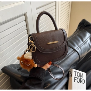 Détail d'un sac selle en cuir marron foncé avec barre dorée et pendentif en peluche