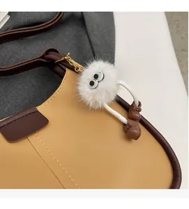 Close-up of a cute white plush ball charm with bow shoes on a stylish shoulder bag