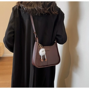 Detail of dark brown shoulder bag with a cute white plush monster pendant on the side