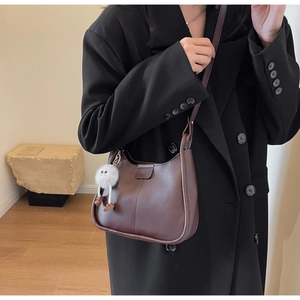 Detailed view of deep brown crescent shoulder bag with white plush monster charm accessory