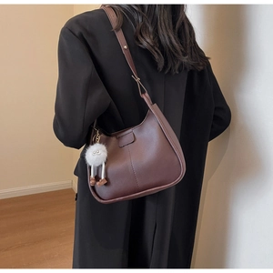 Brown semi-circle crossbody bag with decorative stitching and a cute plush doll charm