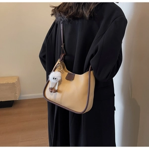 Side view of a light brown hobo bag with dark brown trim and a cute fuzzy charm