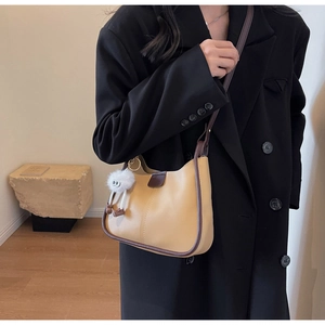 Chic khaki bucket bag with brown trim and cute plush charm on a black blazer