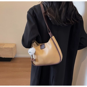 Close-up of minimalist khaki shoulder bag with brown trim and cute white plush charm