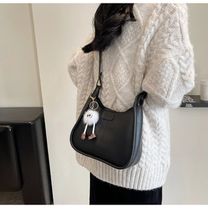 Detail of black crescent shoulder bag in matte leather with a plush charm accessory