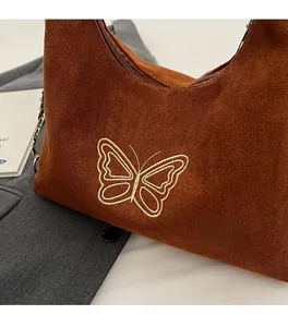 Close-up of brown suede hobo bag featuring white butterfly embroidery and metal chain