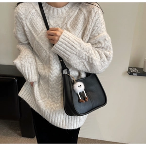 Detail of black leather crossbody bucket bag with white plush monster charm accessory