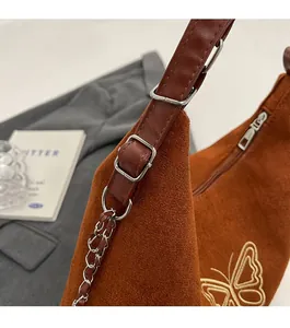 Detail of silver metal buckle and chain strap on a brown suede bag with yellow embroidery