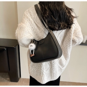 Classic black leather shoulder bag with white pom-pom pendant shown on model's shoulder