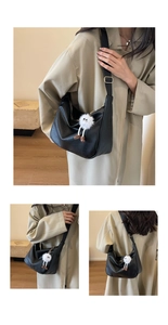 Detail of black lychee texture PU leather bag with wide strap and plush monster charm
