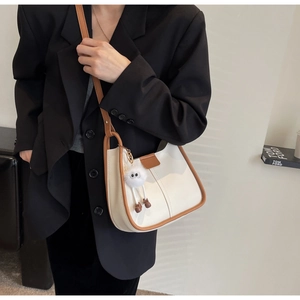 Detail of a minimalist cream shoulder bag with brown leather trim and a plush charm