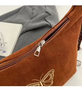 Close-up of smooth metal zipper and butterfly embroidery on brown suede handbag