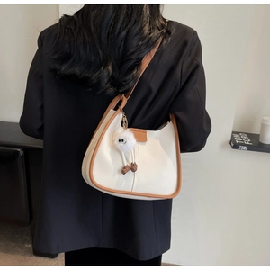 Detail of cream and brown half-moon shoulder bag with fluffy monster charm and smooth leather