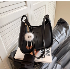 Detail of a black crescent tote bag featuring a cute white plush monster charm