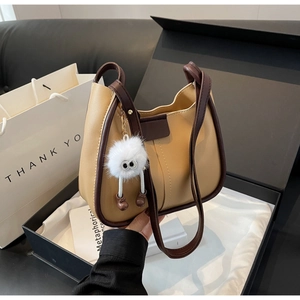 Oatmeal and brown leather tote bag with plush charm inside a stylish black gift box
