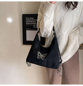 Detail of golden butterfly embroidery on a black suede tote bag with metal chain strap