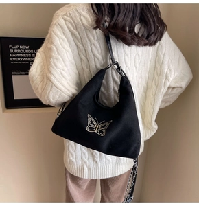 Detail of black hobo bag featuring golden butterfly embroidery and metal chain strap