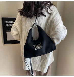 Detail of black curved tote with golden butterfly decor and metallic chain strap