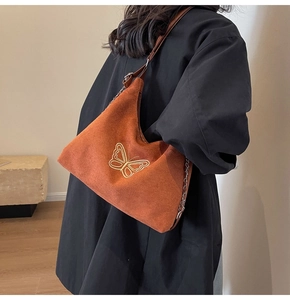 Close-up of brown suede shoulder bag with gold butterfly embroidery and chain strap