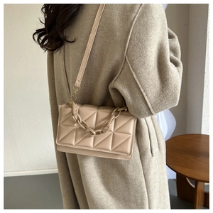 Sac bandoulière matelassé beige avec chaîne en résine porté par un mannequin en studio