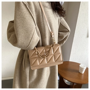 Sac à bandoulière matelassé beige avec chaîne épaisse porté par un mannequin au café