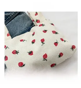 Detail of white corduroy tote bag featuring red strawberry embroidery on denim fabric