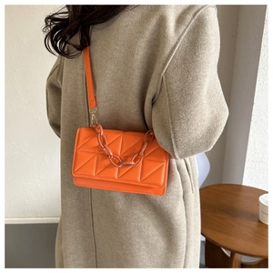 Détail d'un sac bandoulière matelassé orange avec grosse chaîne porté sur un manteau