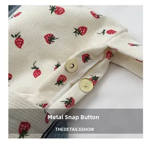 Detail view of the golden magnetic snap closure on a strawberry print corduroy tote bag