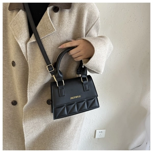 Detail of black crossbody bag with geometric triangle patterns on a beige wool coat