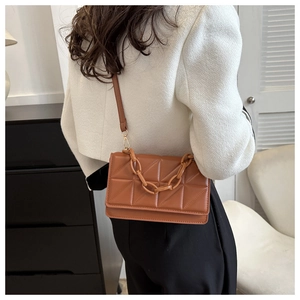 Détail d'un sac bandoulière en cuir marron avec matelassage géométrique et chaîne décorative