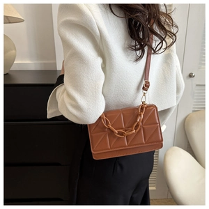 Détail du sac bandoulière matelassé marron avec chaîne en résine sur manteau blanc