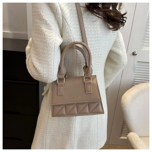 Detail view of beige crossbody bag with quilted texture and gold lettering hardware