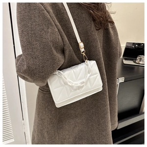Détail d'un sac bandoulière blanc matelassé avec chaîne dorée sur un manteau marron