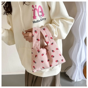 Detail of pink corduroy handbag featuring all-over red strawberry print and sturdy dual handles