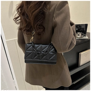 Détail d'un sac bandoulière matelassé noir avec chaîne en résine et bandoulière en cuir