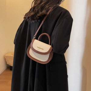 Sac selle chic beige et marron avec boucle dorée présenté sur un mannequin en tailleur