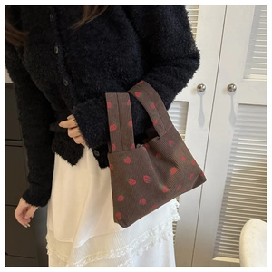 Gros plan d'un sac à main en velours côtelé marron avec des motifs de fraises rouges