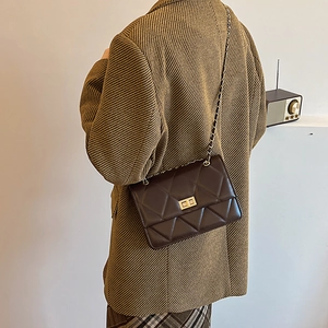Sac à bandoulière matelassé marron foncé avec fermoir doré porté par un mannequin