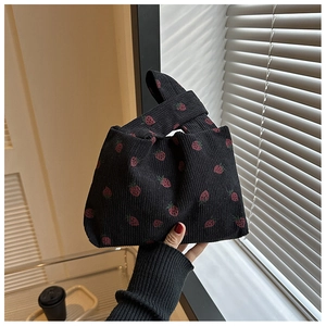 Détail de l'imprimé fraise sur le sac à nœud en velours côtelé noir porté à la main