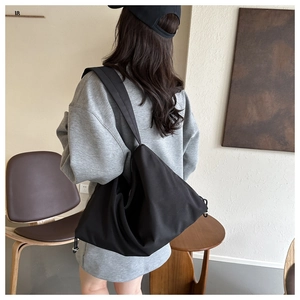 Close-up of black crossbody dumpling bag with wide shoulder strap and drawstring detail