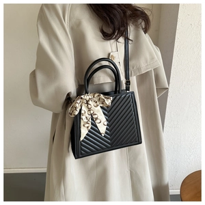 Detail of black quilted shoulder bag with decorative scarf and elegant silk strap handle
