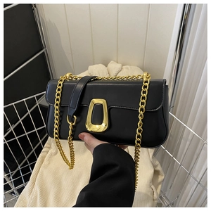 Detail of black leather flap crossbody bag with chunky gold chain and geometric buckle