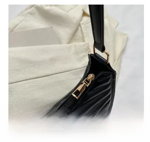 Detail of smooth gold zipper and black pleated texture on minimalist shoulder bag