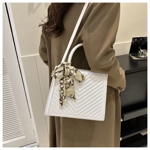 Close-up of a white V-quilted faux leather tote bag with a silk scarf tied on the handle