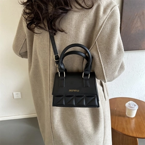 Sac bandoulière matelassé noir avec détails dorés porté sur un manteau en laine