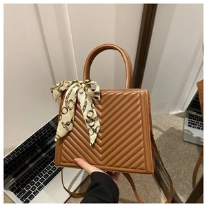 Detail of caramel brown V-quilted faux leather handbag with decorative silk scarf handle