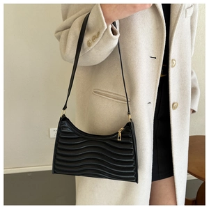 Close-up of black textured underarm bag with wave pleats and gold metal hardware